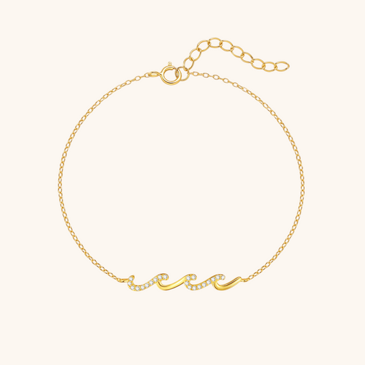Thin gold bracelet with wave-shaped crystal detail, laid flat on white background