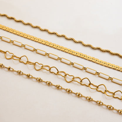 Close-up of gold wavy and heart link necklaces styled as chokers, resistant to water.