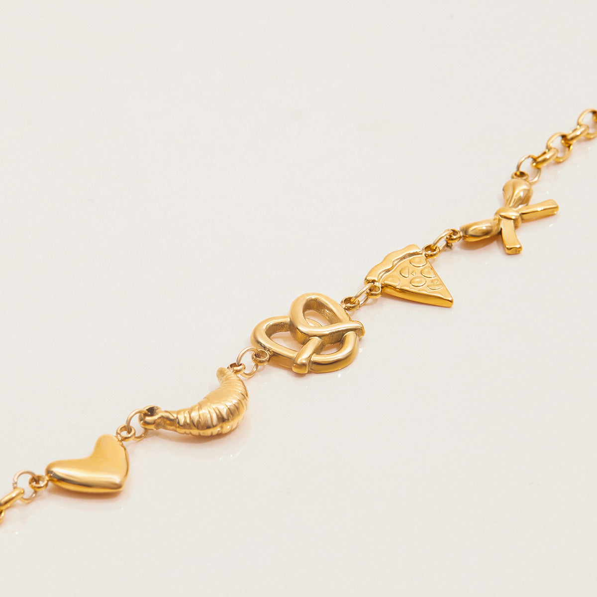 Fun gold bracelet with heart, croissant, pretzel, pizza, and bow charms