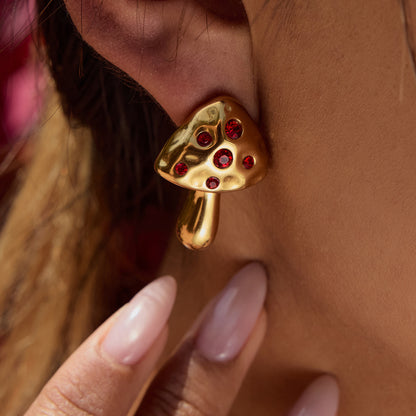 Model wearing gold toadstool earrings with red stones