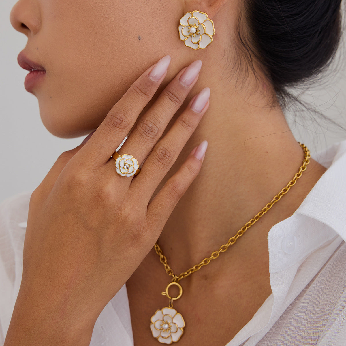 Model wearing matching white enamel flower earrings, necklace and ring with gold finish