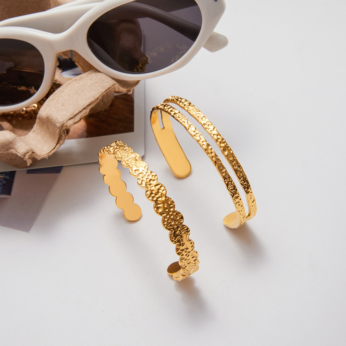 Gold bracelets on a white surface with sunglasses in the background