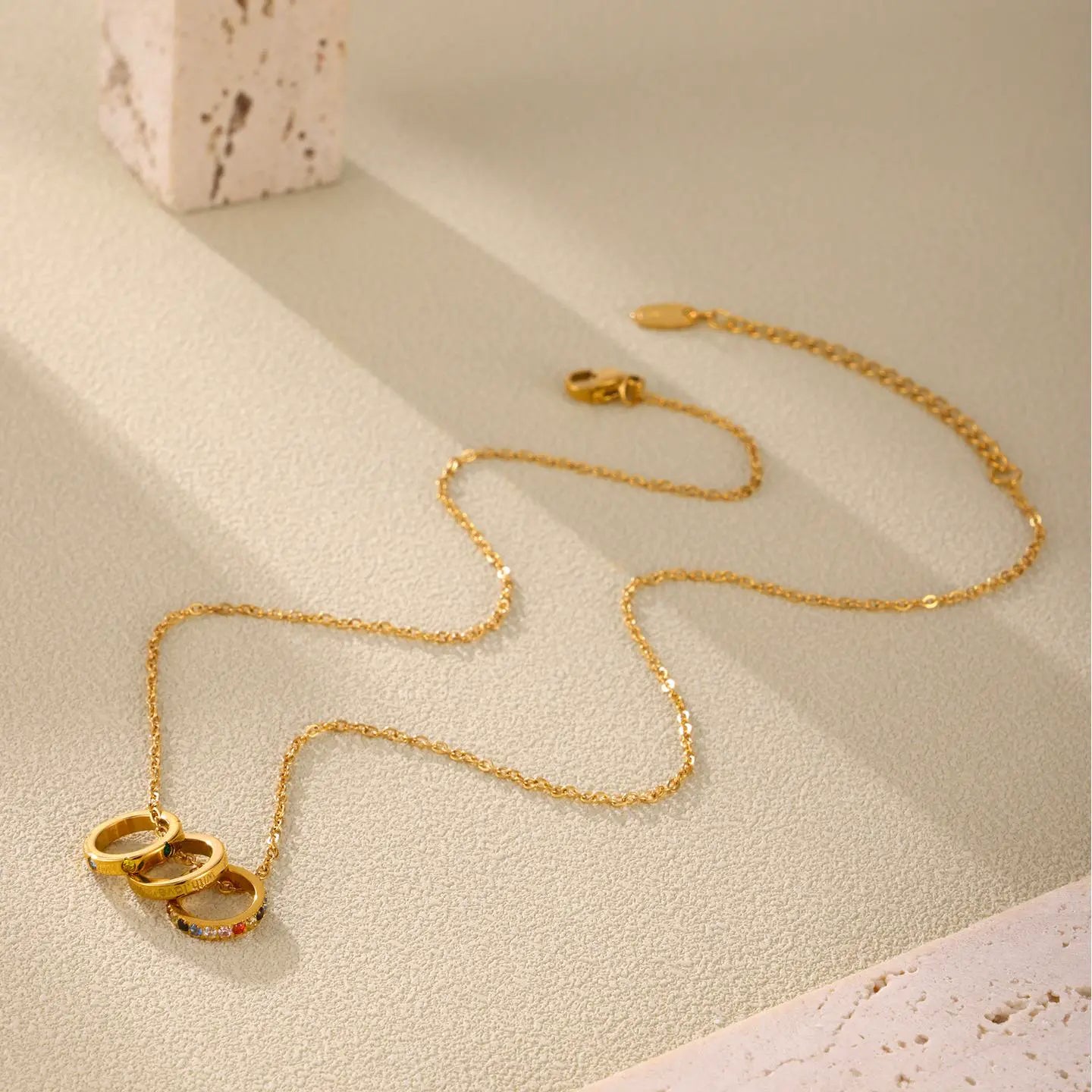 Detailed display of the 'With Love' Triple Ring Necklace, featuring multicolor zircon stones, laid out with the stainless steel chain for a stylish look.