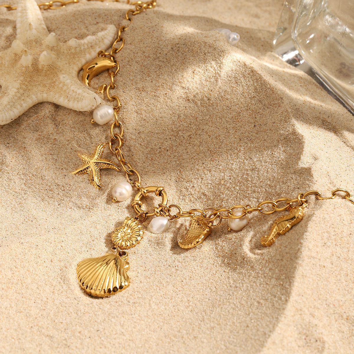 Shell and ocean charm gold necklace photographed on beach sand with starfish
