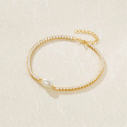 Elegant pearl drop bracelet with delicate gold chain on a soft textured surface.