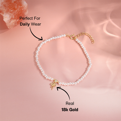 gold-pearl-bracelet-pink-background.png – Stunning pearl bracelet adorned with a 14k gold bow charm, displayed on a soft pink background for an elegant and chic aesthetic.