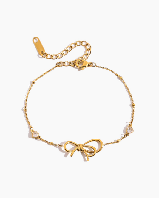 Gold bracelet with bow charm on a white background