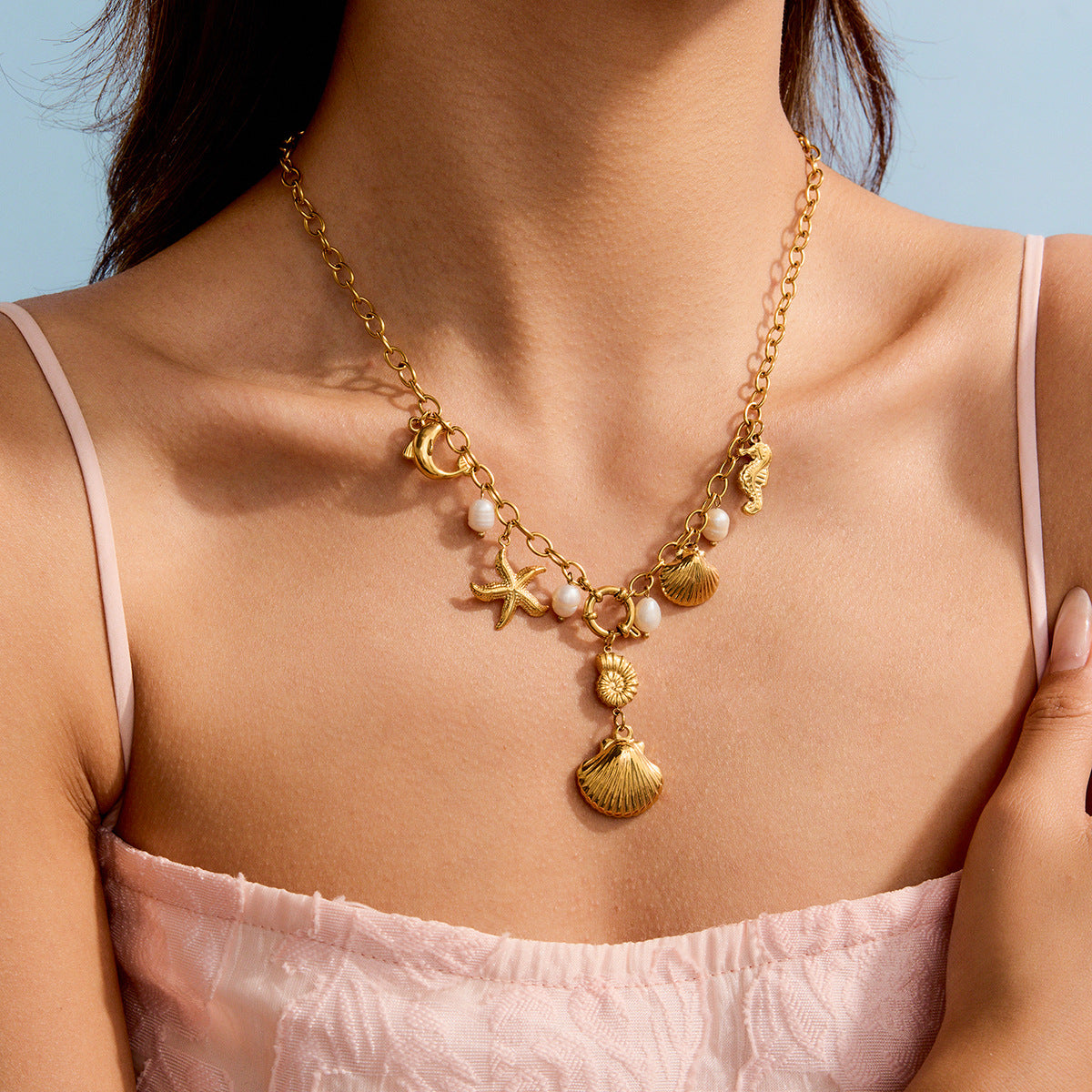 Model wearing gold ocean charm necklace with dangling shell and freshwater pearls