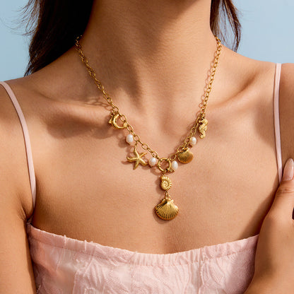 Model wearing gold ocean charm necklace with dangling shell and freshwater pearls