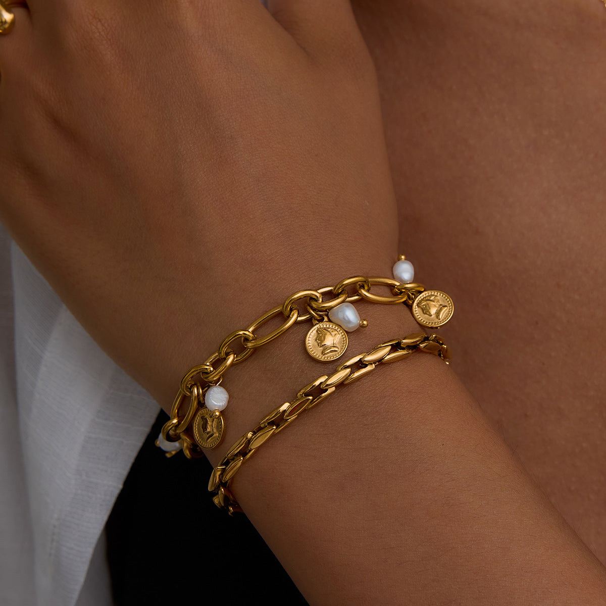 Woman wearing a layered stack of gold chain and coin pearl bracelets, summer jewelry style