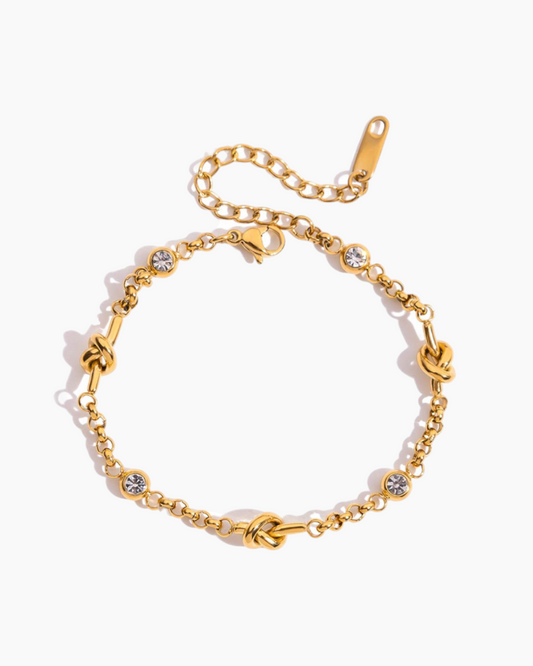 Gold bracelet with knot designs and small crystals on a white background